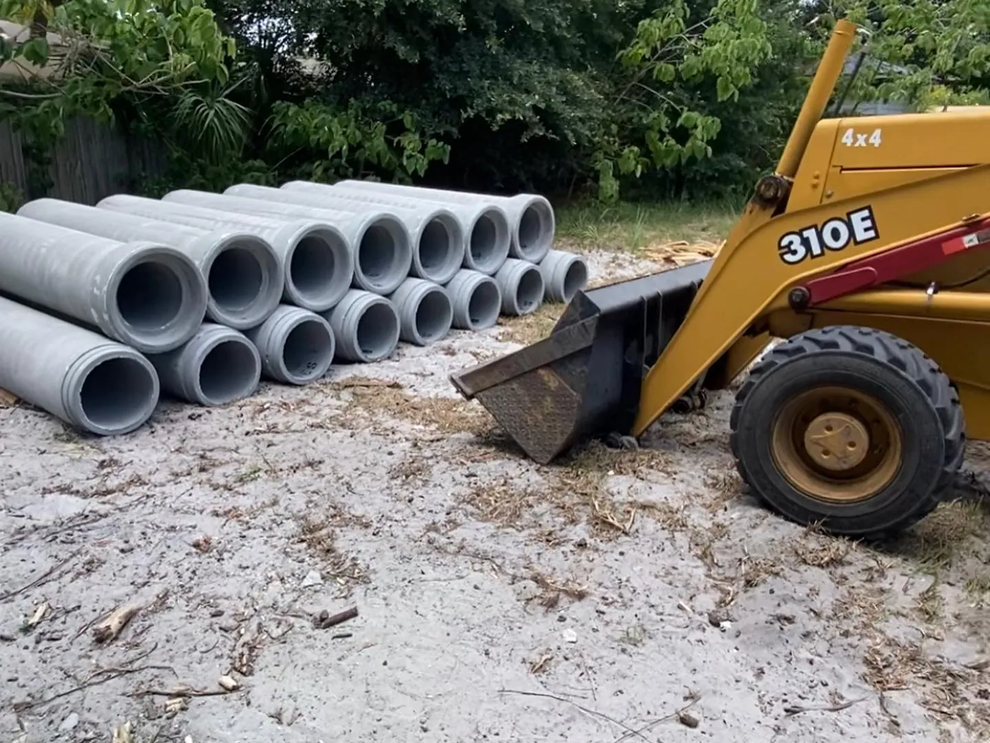 Stacked concrete culvert pipe sections beside a backhoe on a sandy job site