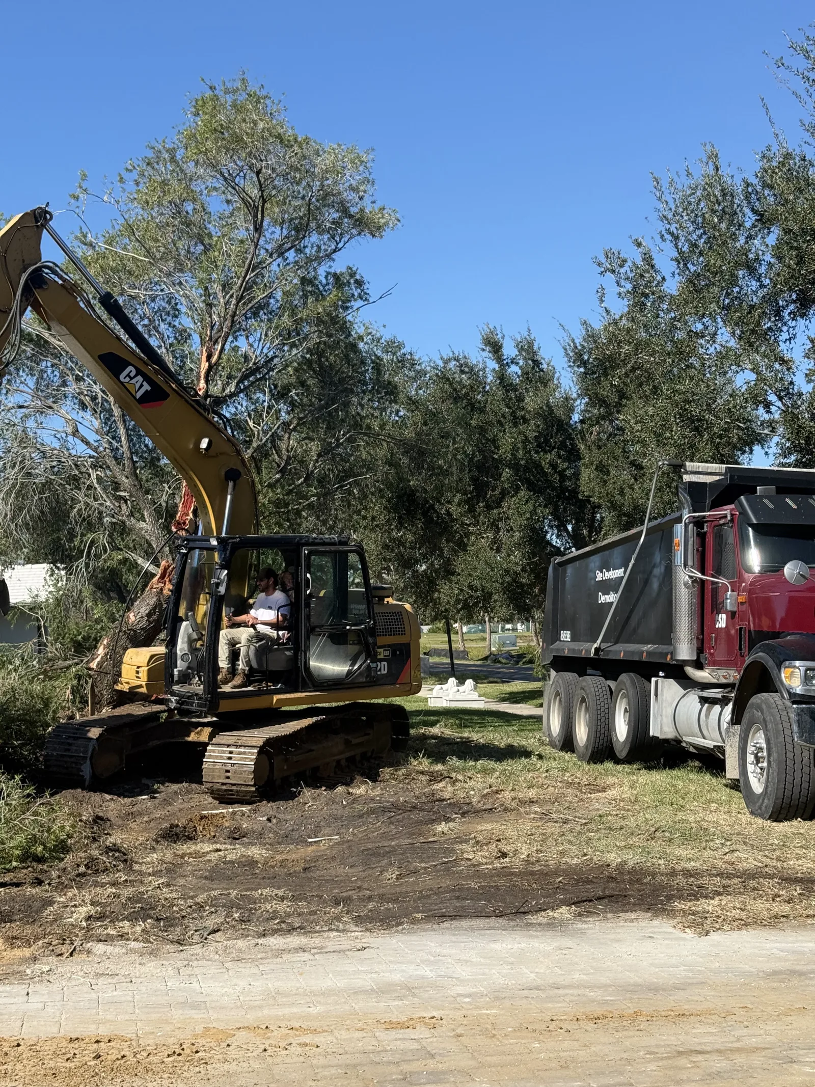 Excavator and dump truck hauling dirt along a residential dirt road
