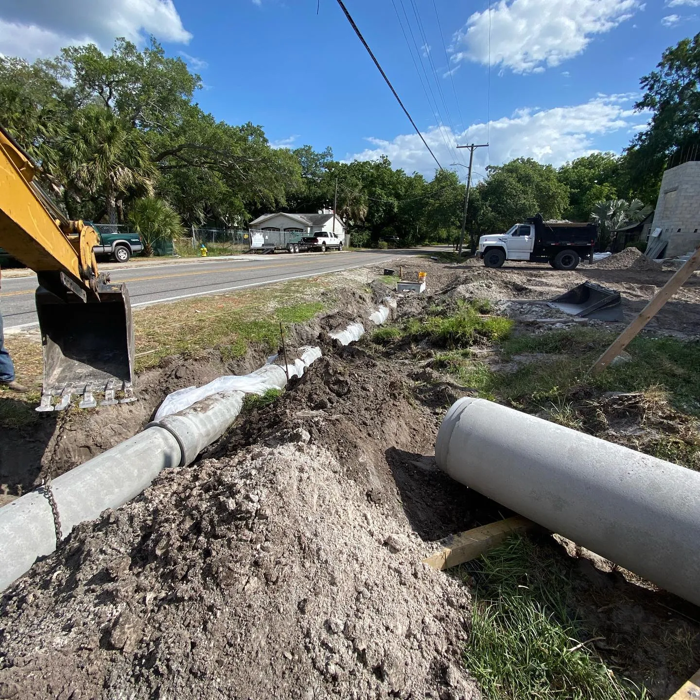 Concrete culvert pipe laid along a roadside ditch, with a backhoe at the open trench