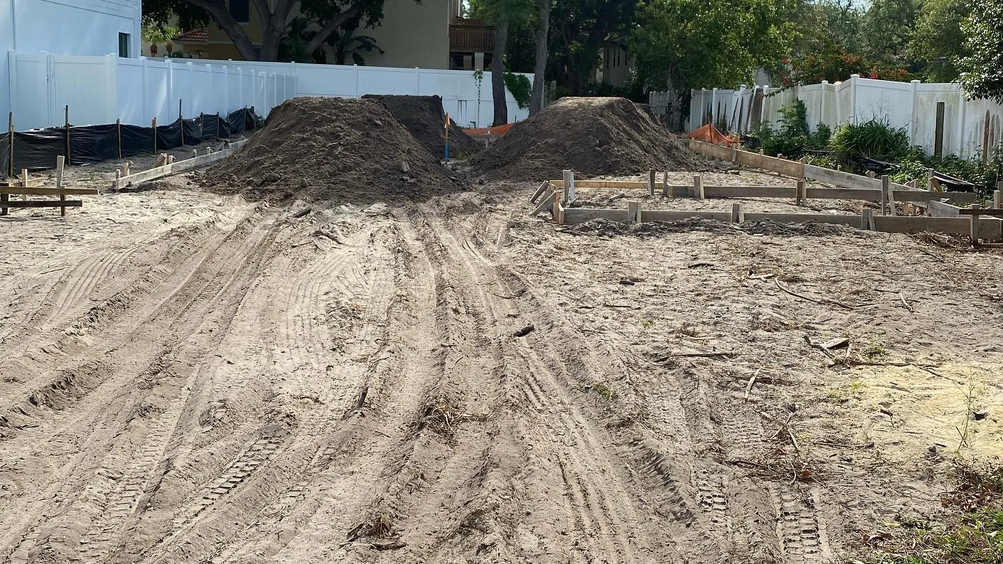 Two dirt piles and machine tracks on a sandy lot with wood forms set for a new home