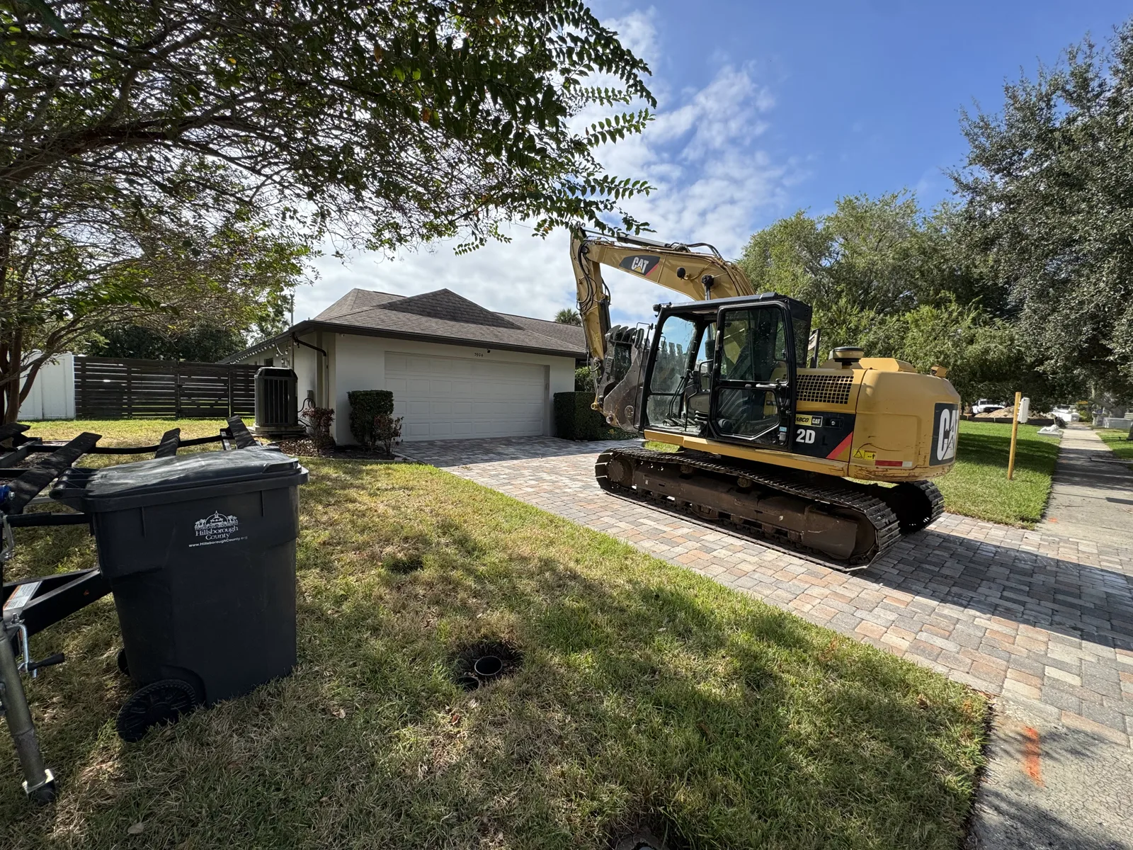 Excavator staged on the driveway beside a garage before demolition