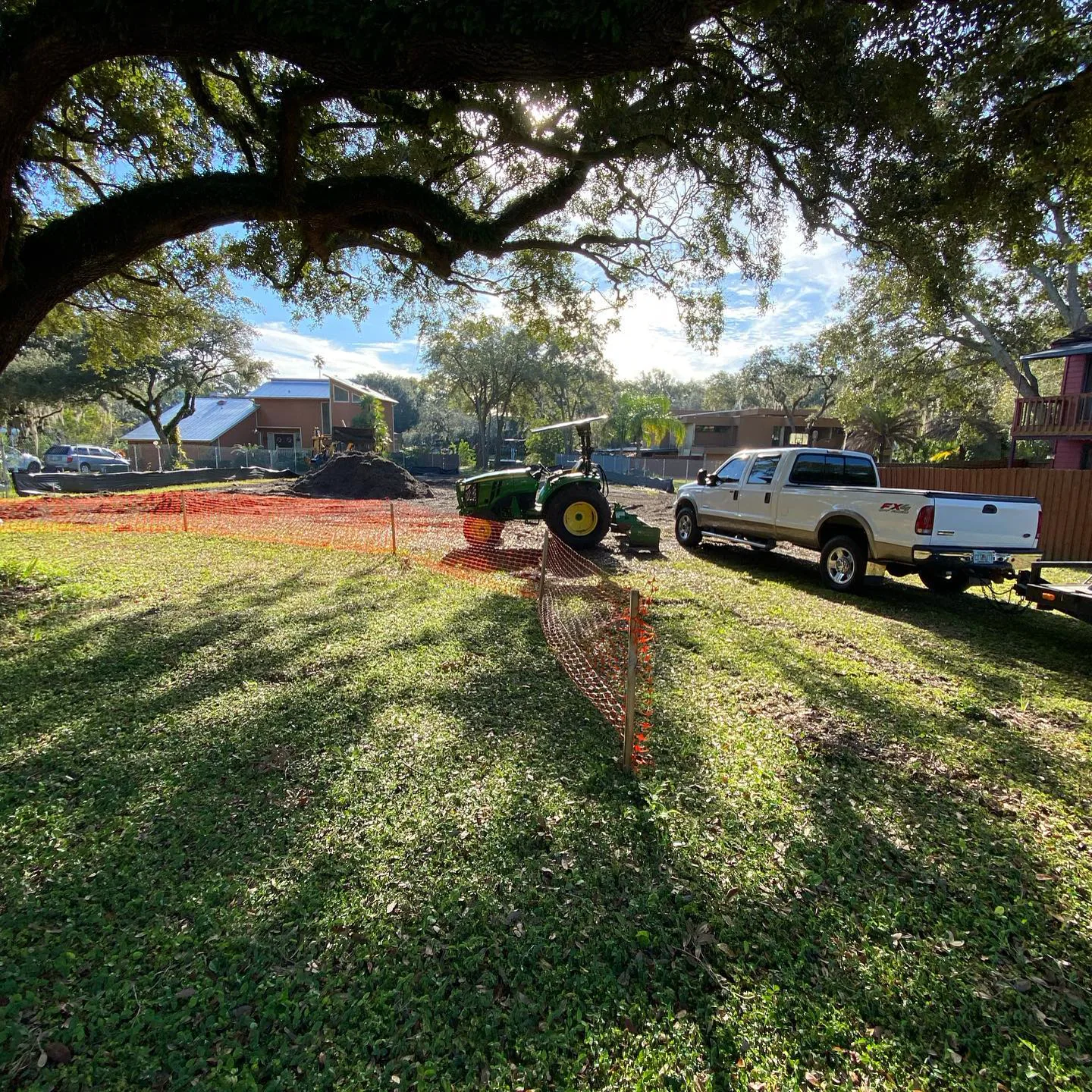 Cleared lot with silt fence up and a compact tractor working near the street