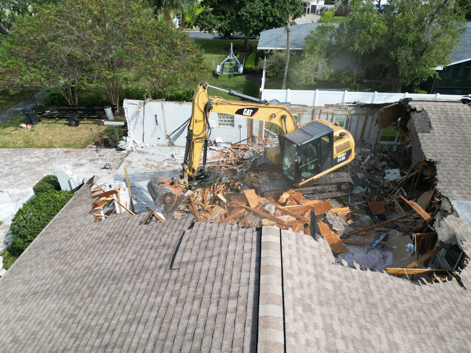 Excavator working through a partially demolished house on a residential lot