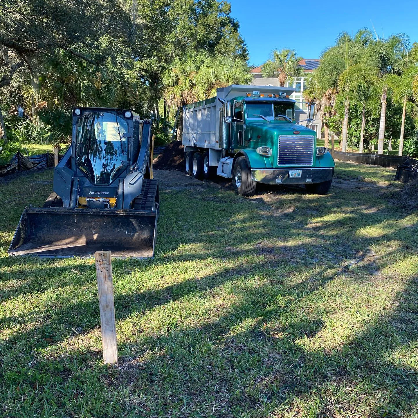 Skid steer and dump truck working together on a residential lot