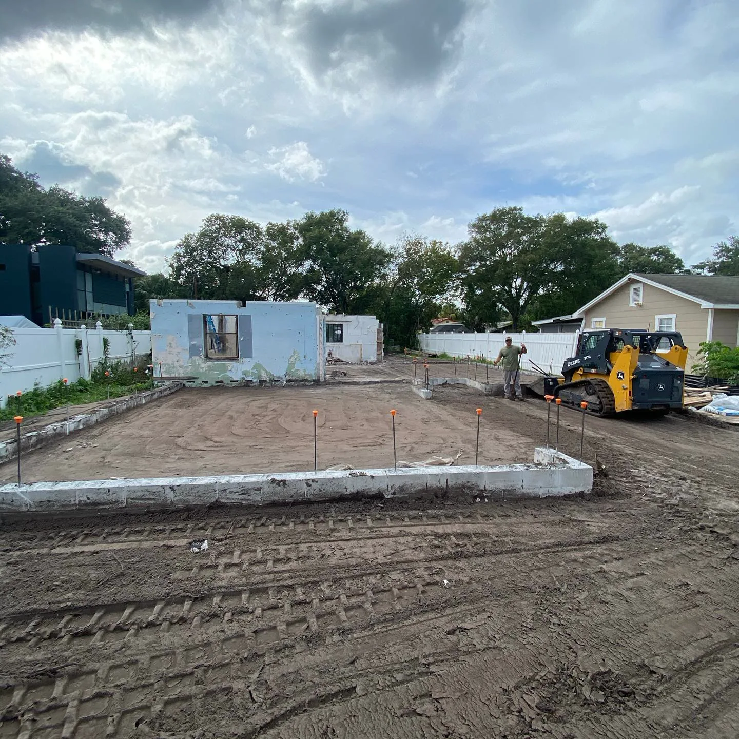 Skid steer clearing a teardown site down to the slab with one wall section still standing